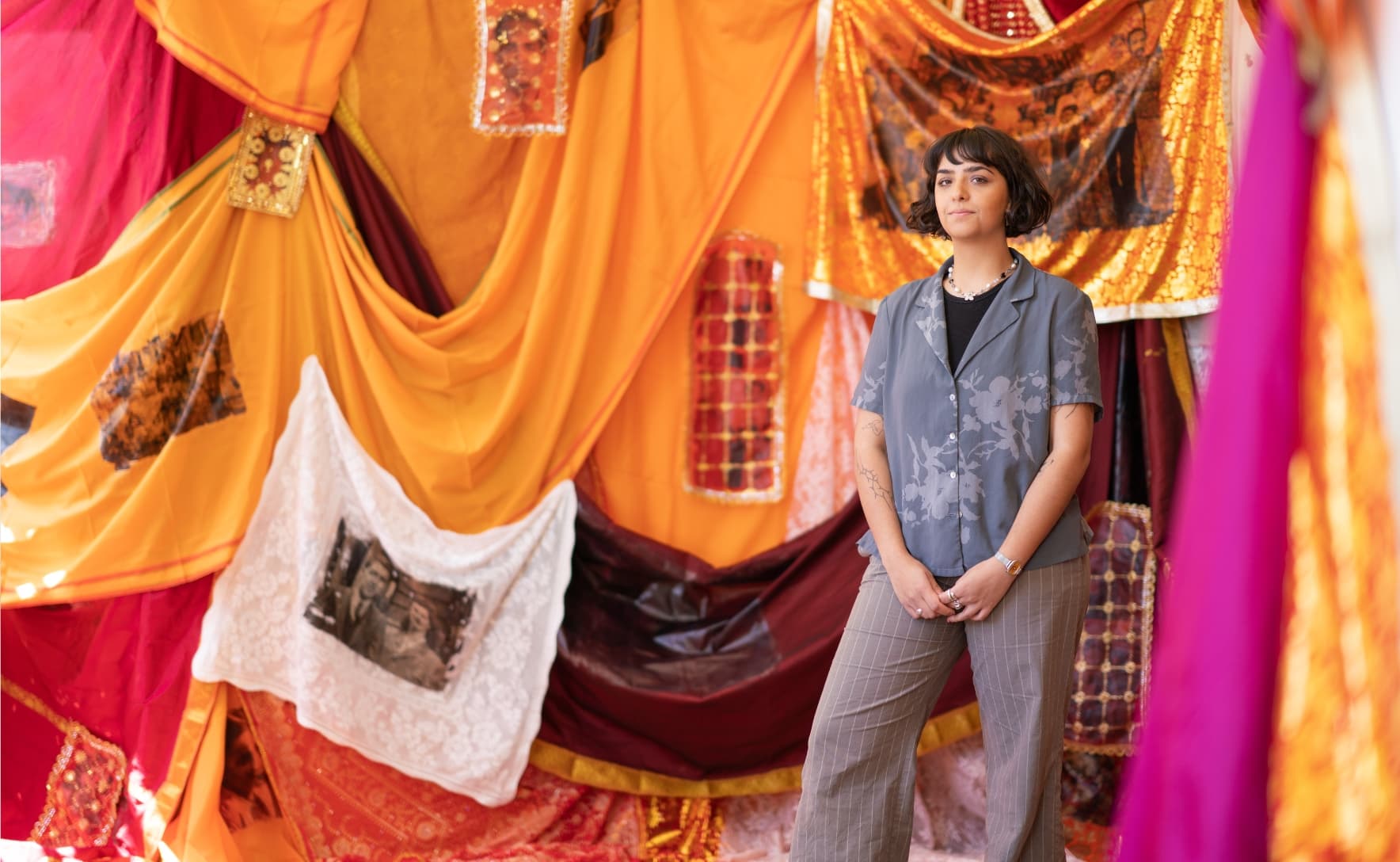 a woman is standing in front of red, orange and white draped fabric including saris and doilies