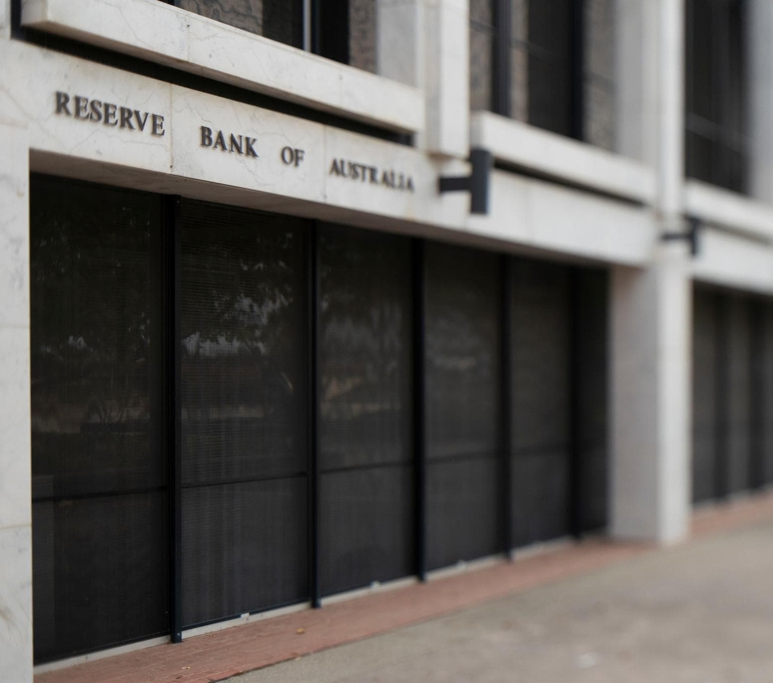 Side angle view of the side of a building. There is lettering on the building that reads Reserve Bank of Australia. The budiling has grey stone and black glass panels