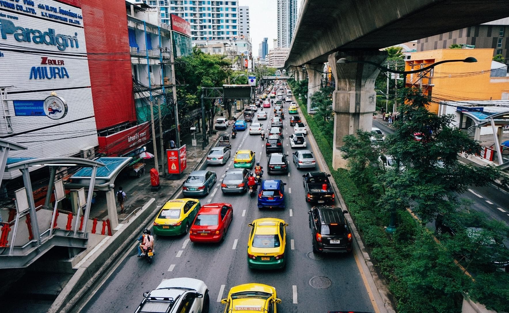 aerial view of a street filled with cars. there are buildings to the left and a conctrete bridge to the right of the street