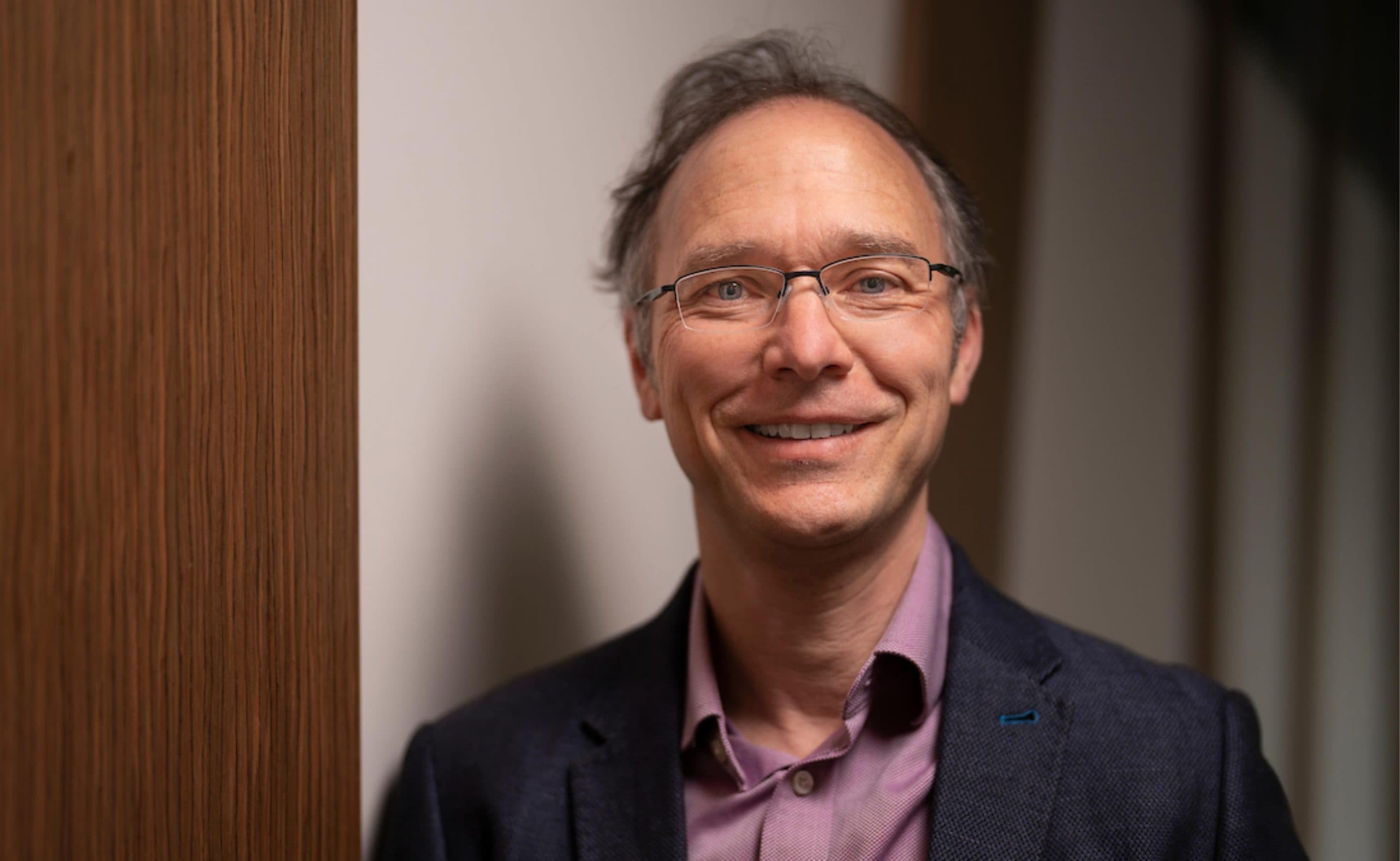 Portrait of Frank Jotzo who wears a dark suit jacket and purple shirt while smiling at the camera.