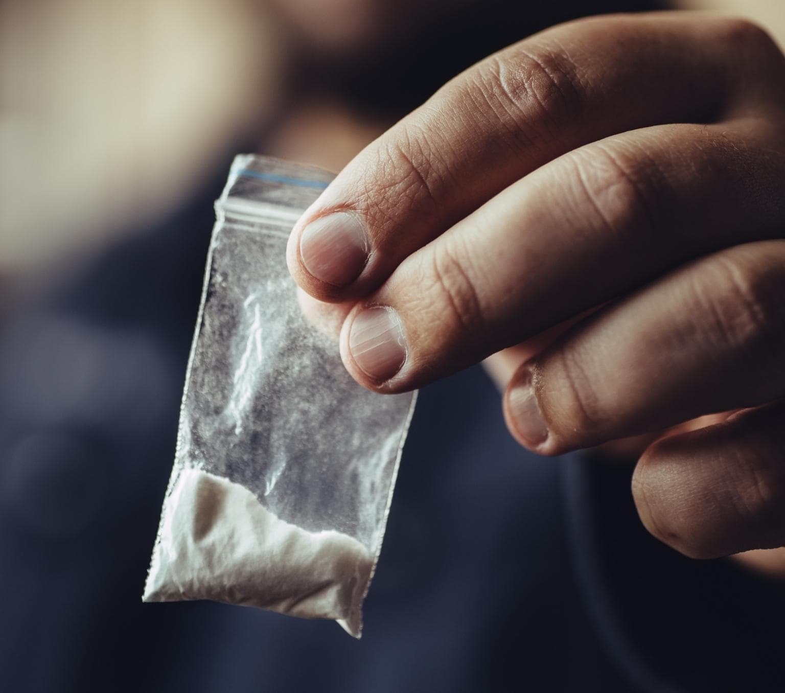 A small ziplock bag containing white powder is held in a person's fingers.