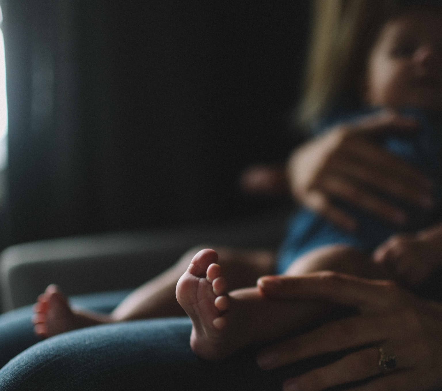 a babies foot is in the foreground and a baby is sitting on its mother's lap