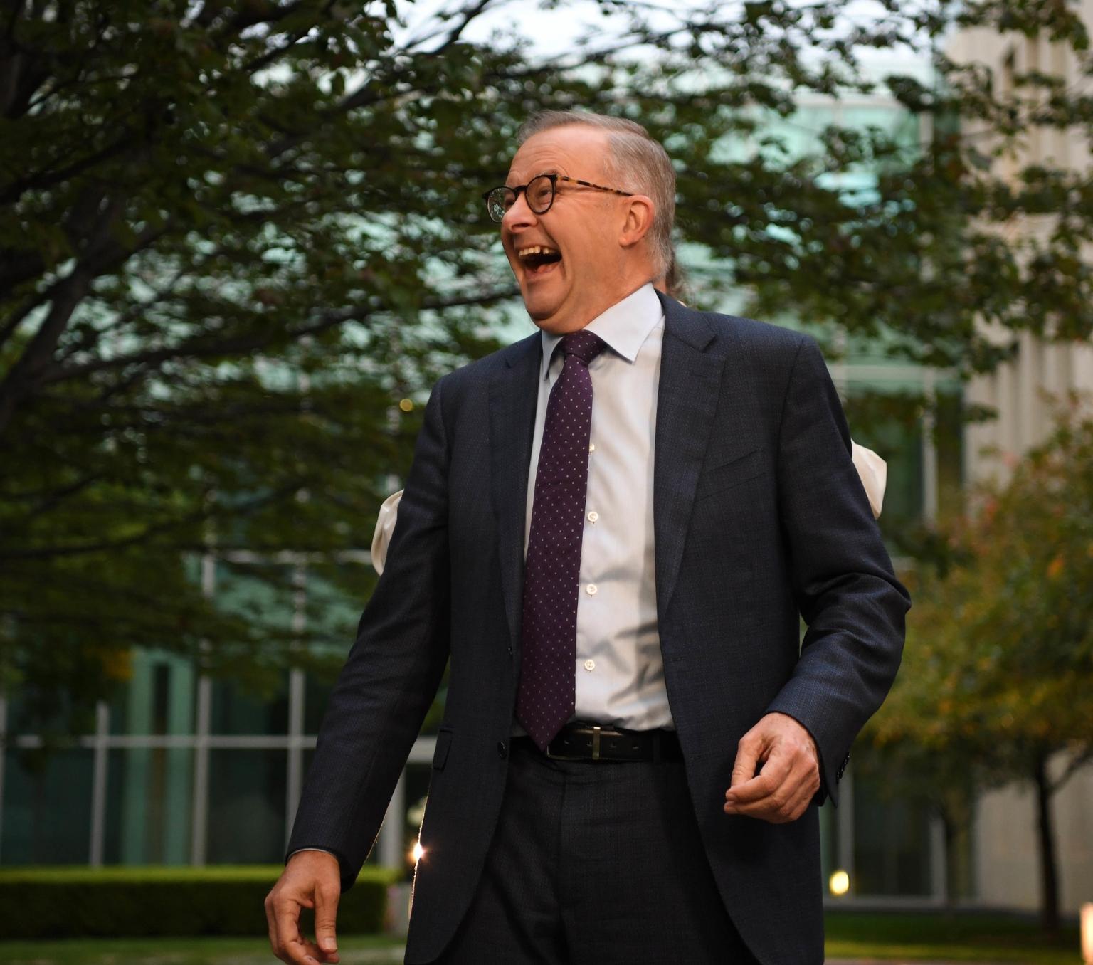 Anthony Albanese is looking to the left of the camera and laughing.