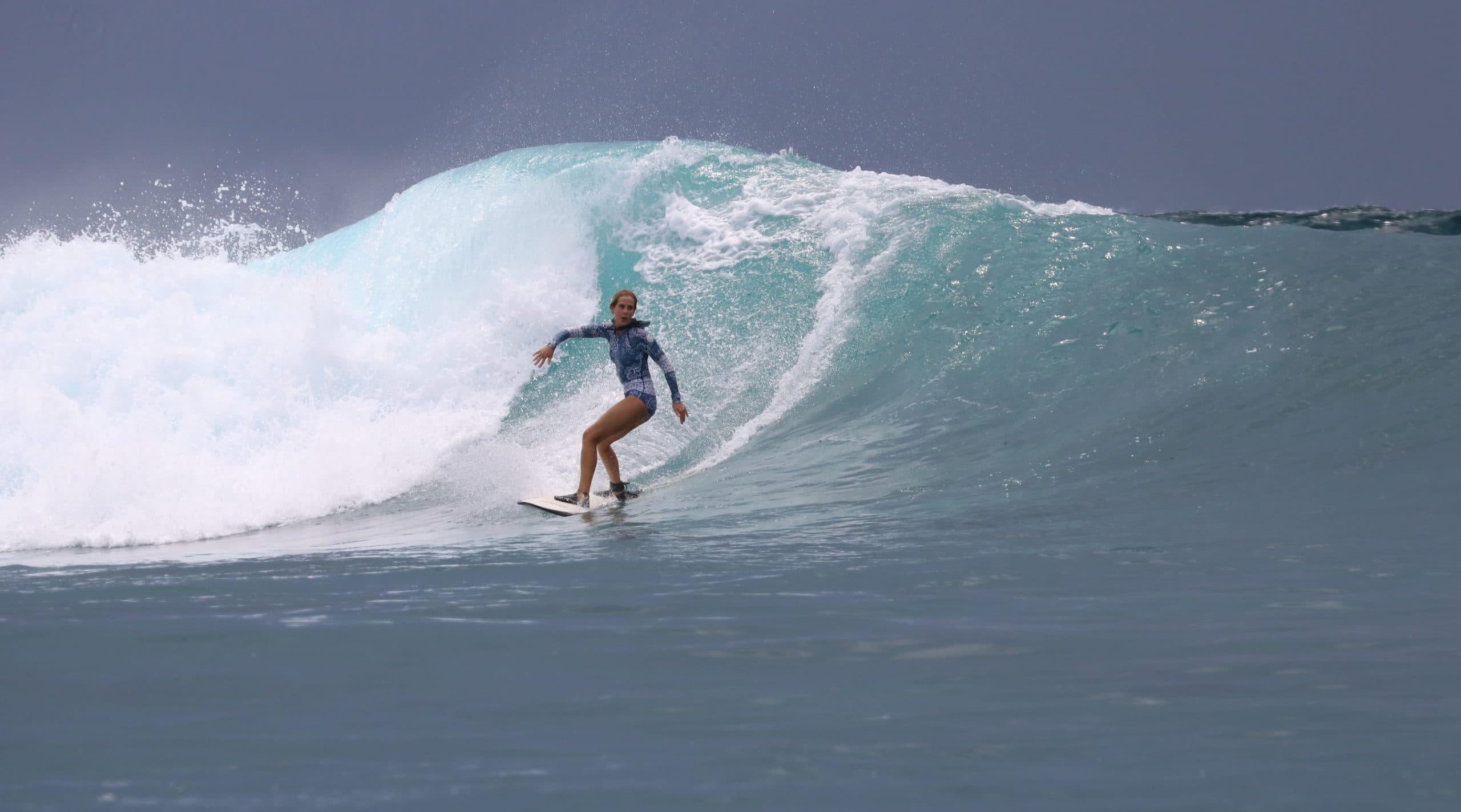 Ana Manero rides a surfboard while a wave breaks behind her.