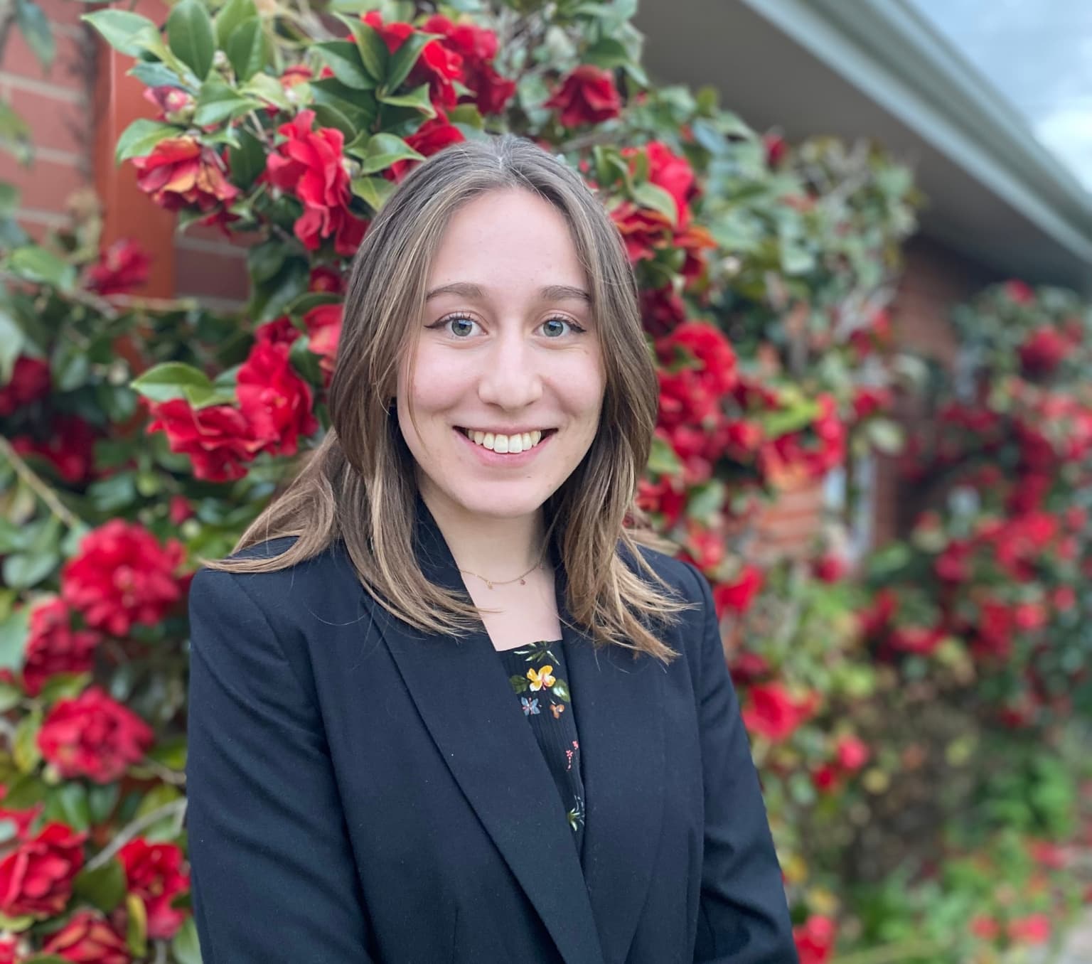 2023 New Colombo Plan scholar Lucy Garner. She is wearing a navy blue blazer and there are red flowers in the background