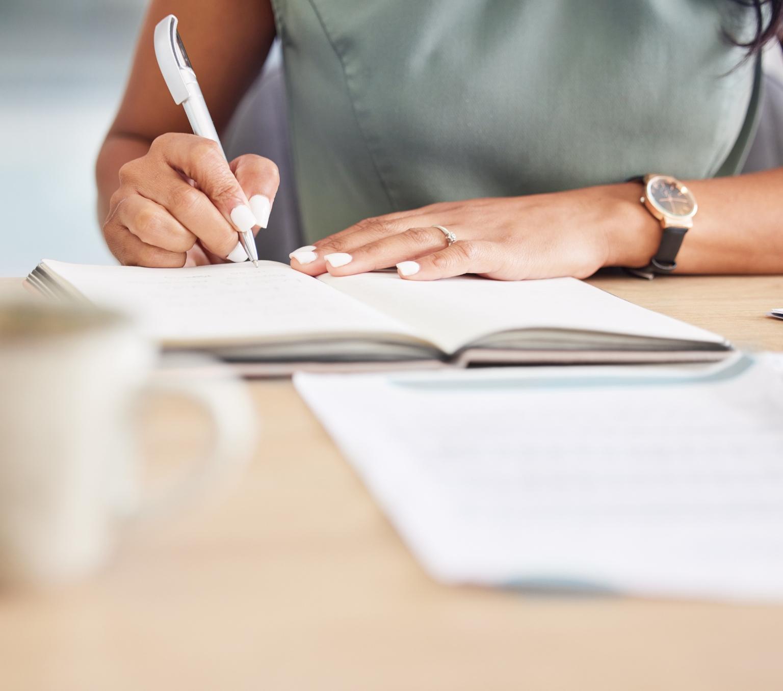 An unidentified female worker sitting at a desk writing in a notepad