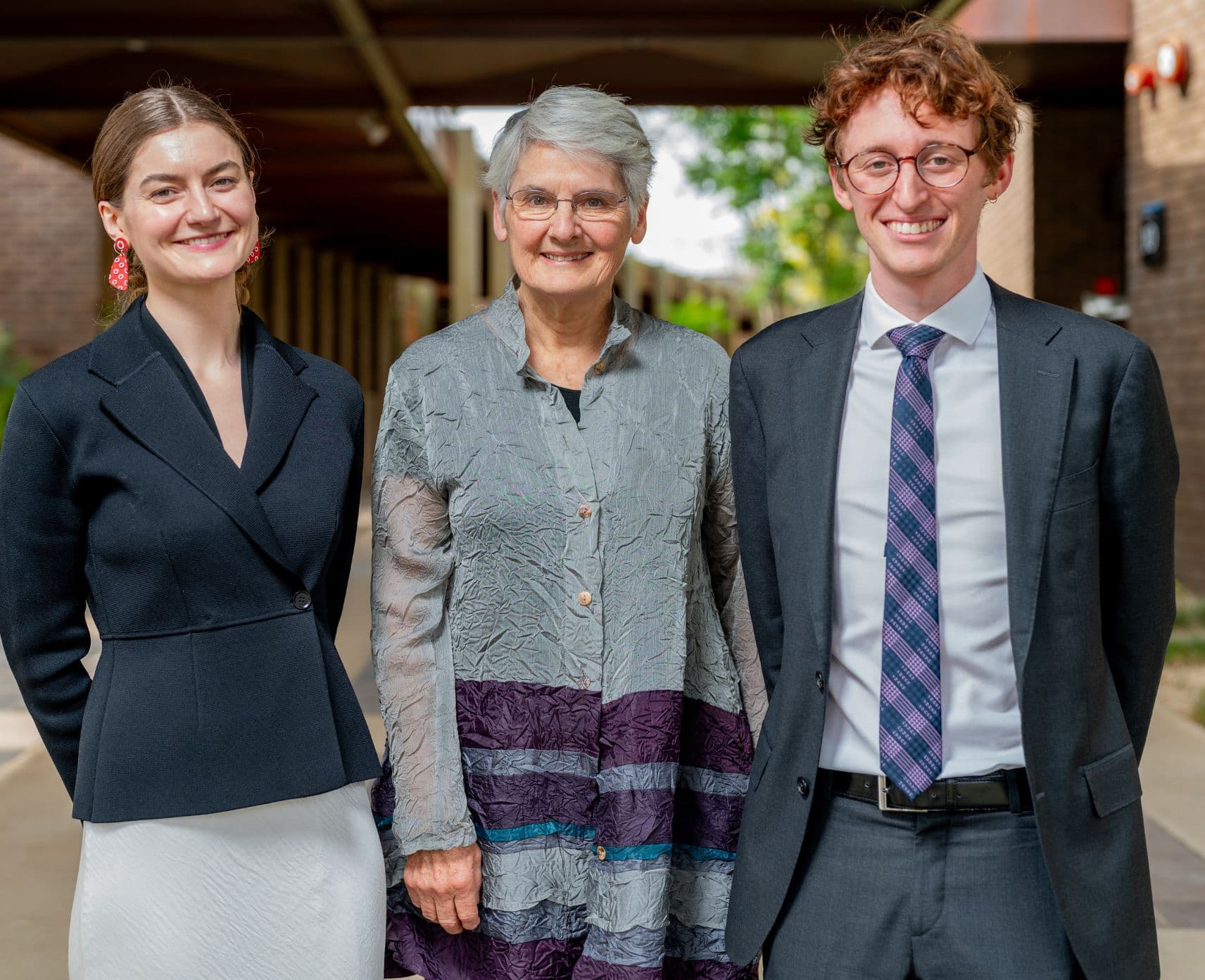 Three people stand shoulder to shoulder smiling.