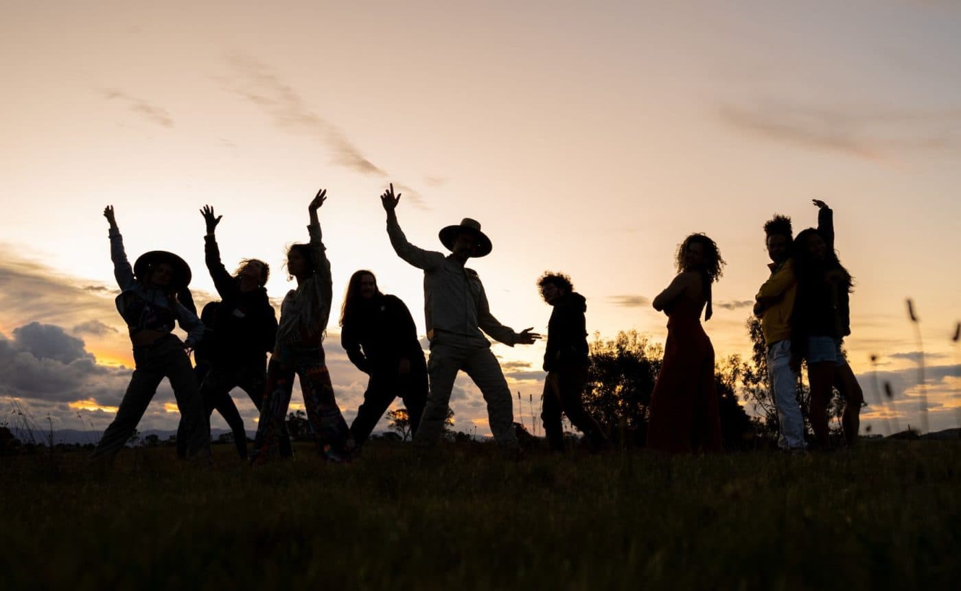 A combination of drag queens, ballet dancers and Brazilian funk dancers wearing colourful costumers filled to the brim with sequins. They are all dancing in a field in regional Victoria.