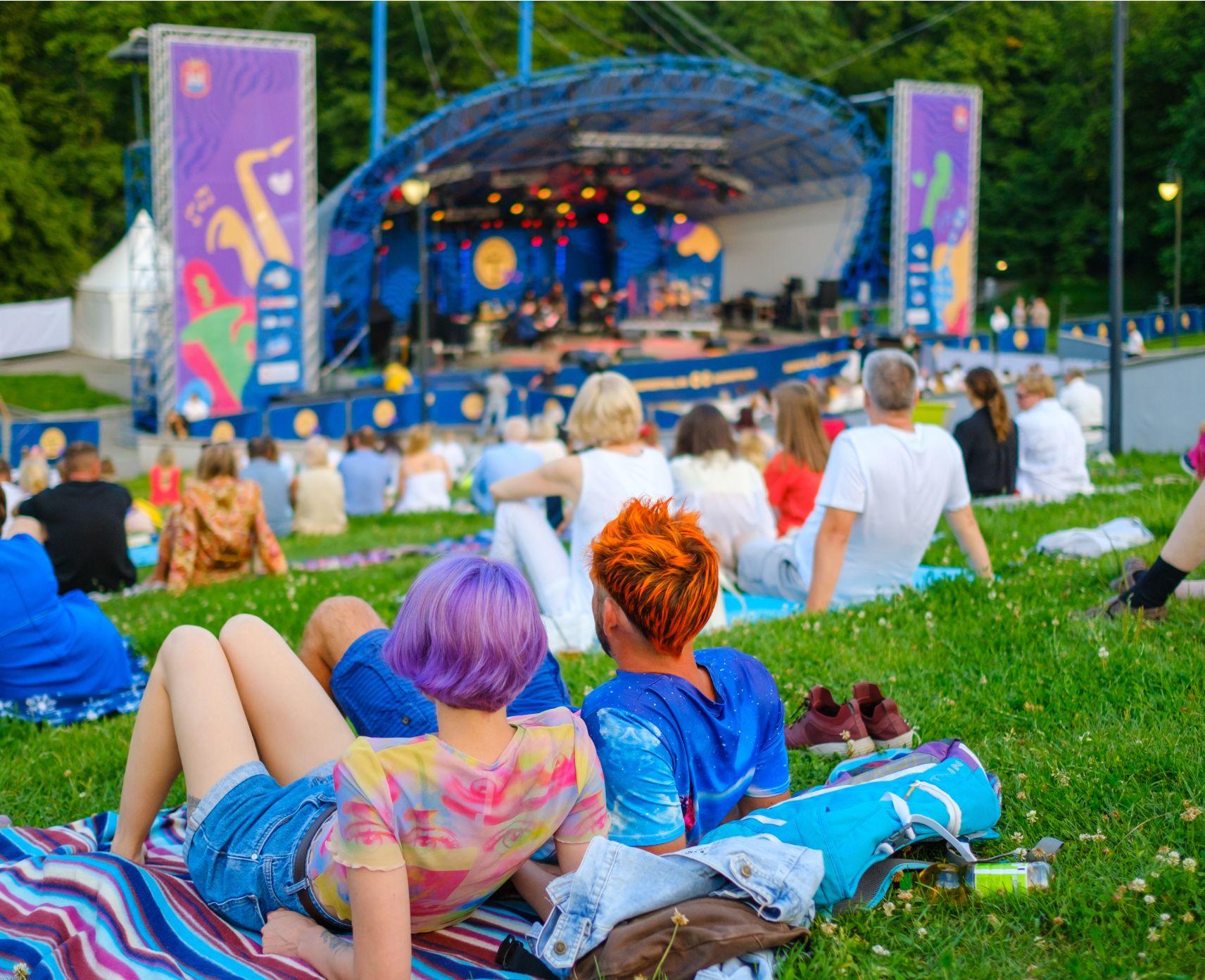 A woman and man sitting on the grass watching a band play music.