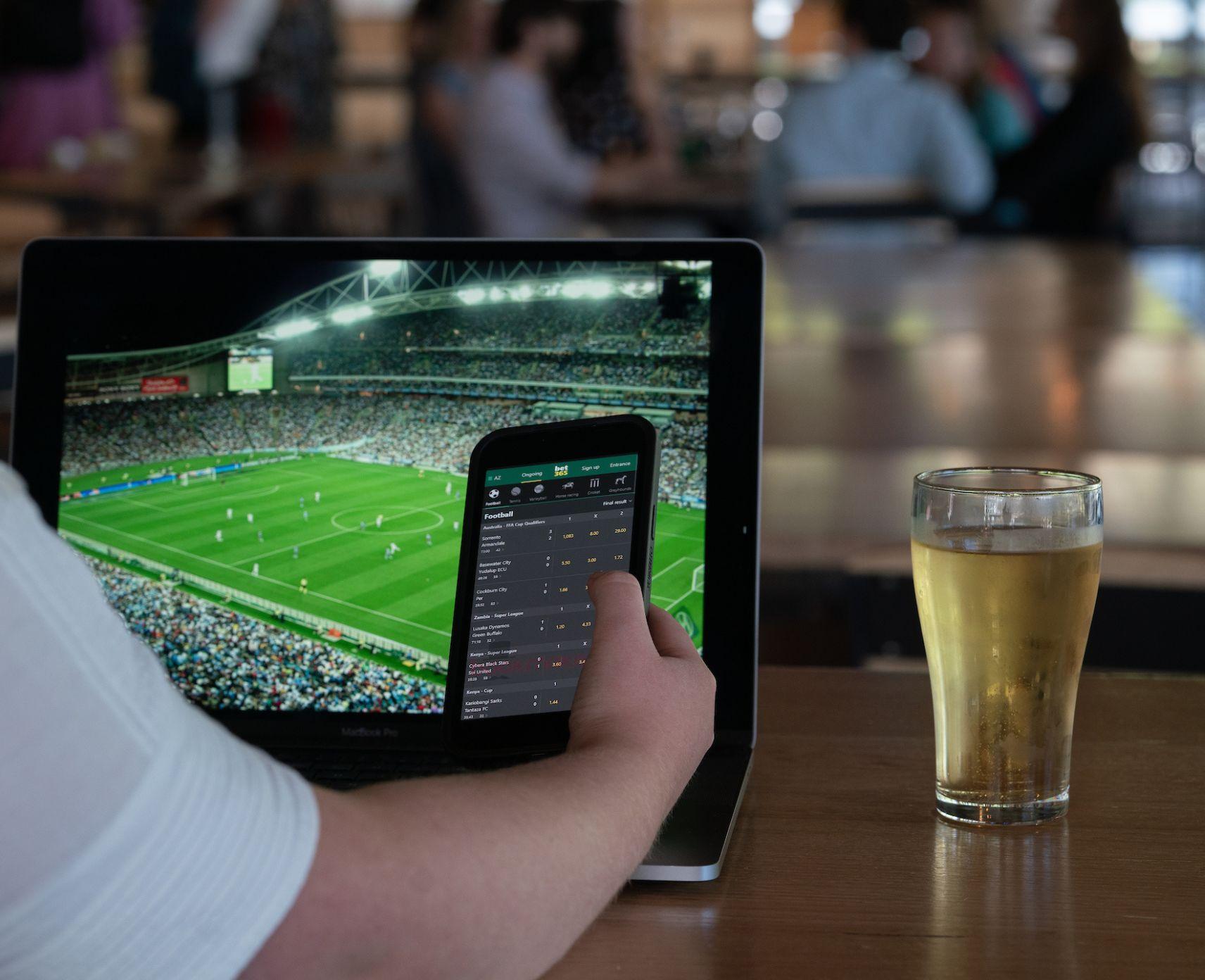 A close up of a person using a sports betting up on their phone while watching a sporting match