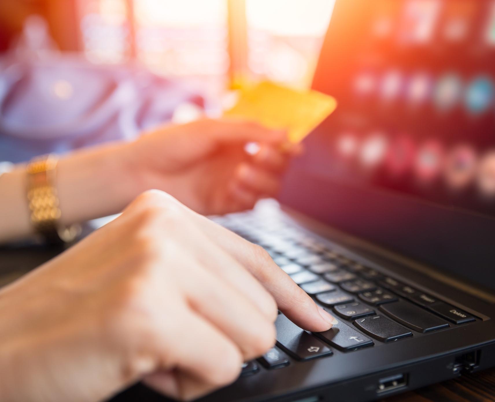 A person holds their credit card in front of a laptop