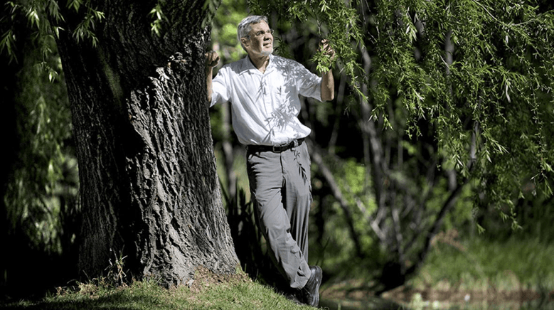 Will Steffen leans against a tree. He's wearing a light shirt and grey pants.