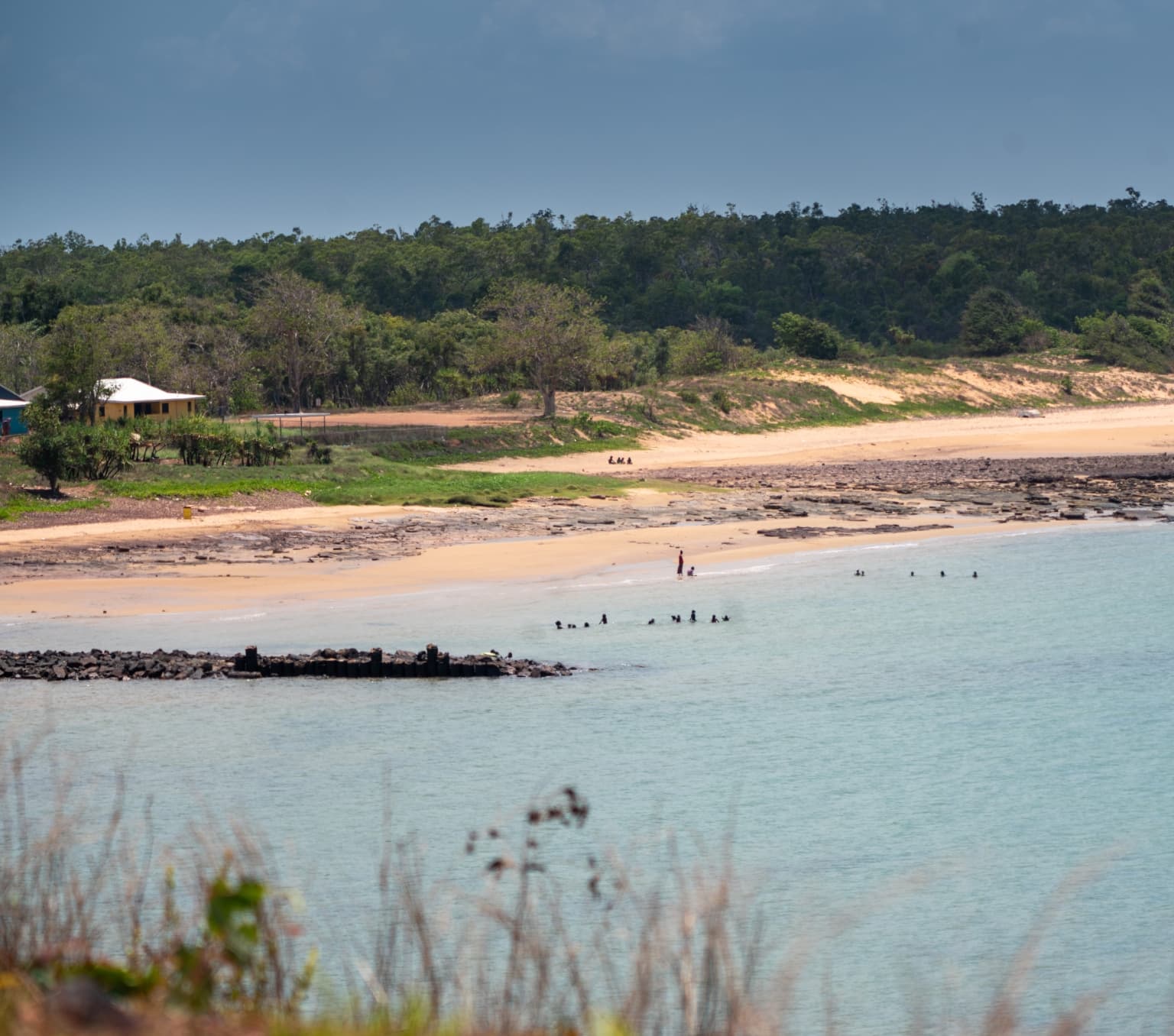 view of a white sandy beach with low tree covered hills behind and aqua blue water