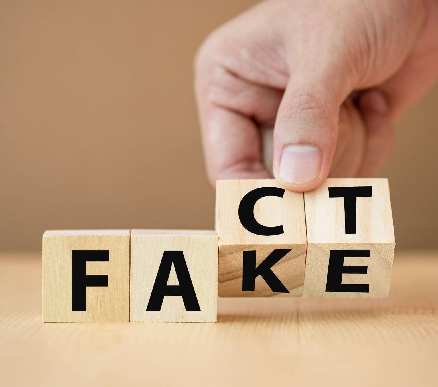 four wooden cudes spelling out the word fact, however the cubes with the letters c and t also show the letters k and e so that the cubes simultaneously spell out fake