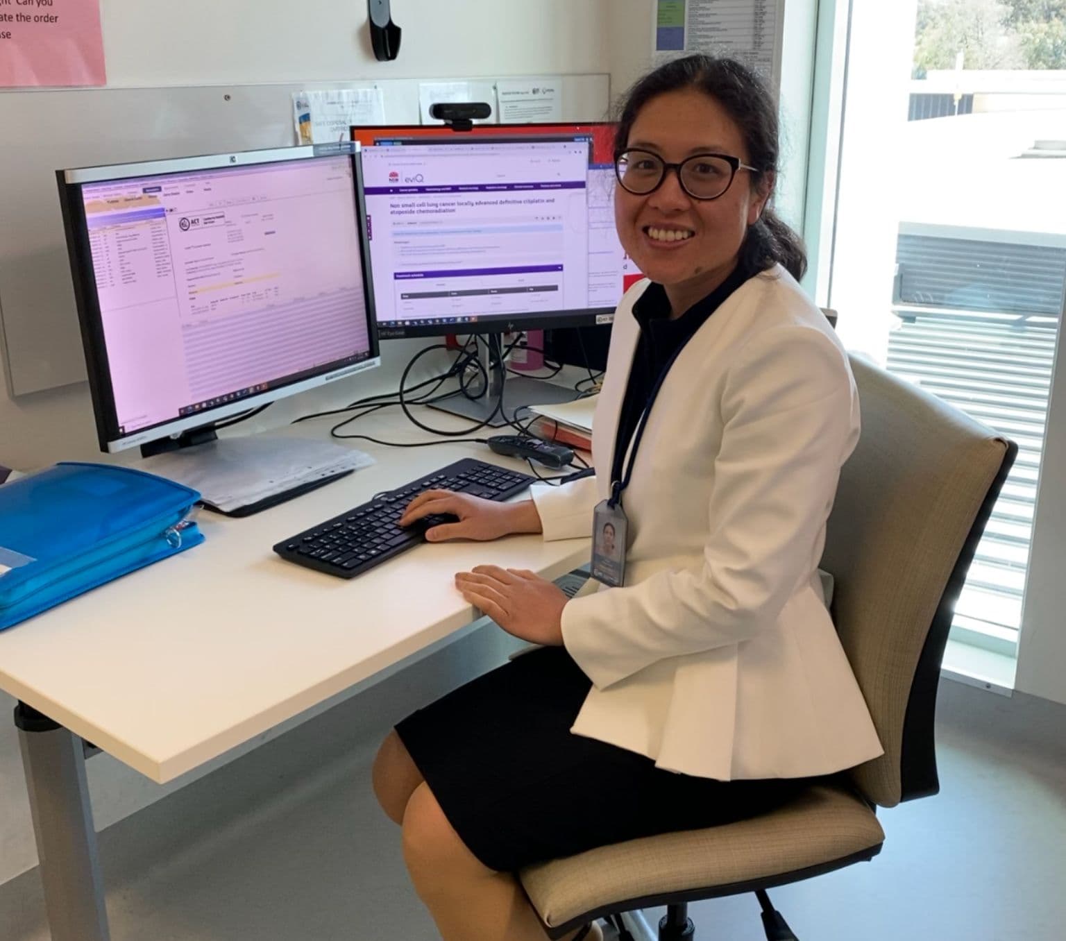 Photo of Dr Yada Kanjanapan sitting at her desk. She is smiling and wearing a white lab coat.