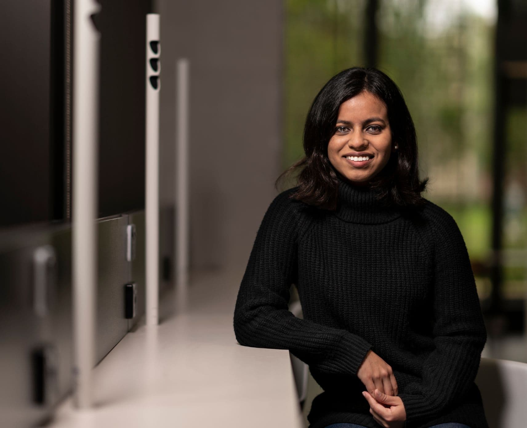 Jessica Rahman leans against a bench. She is smiling and wearing a black top.