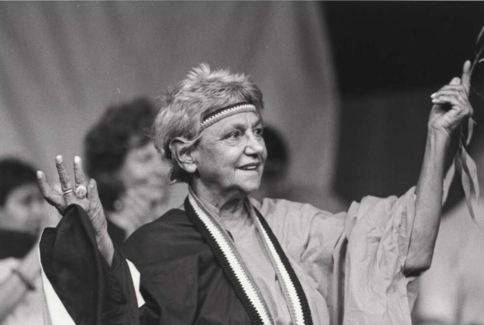 Oodgeroo Noonuccal is pictured in a black and white photo she is smiling and looking away from the camera. She is wearing a wide sleeved loose garmet with a crochet band around her head