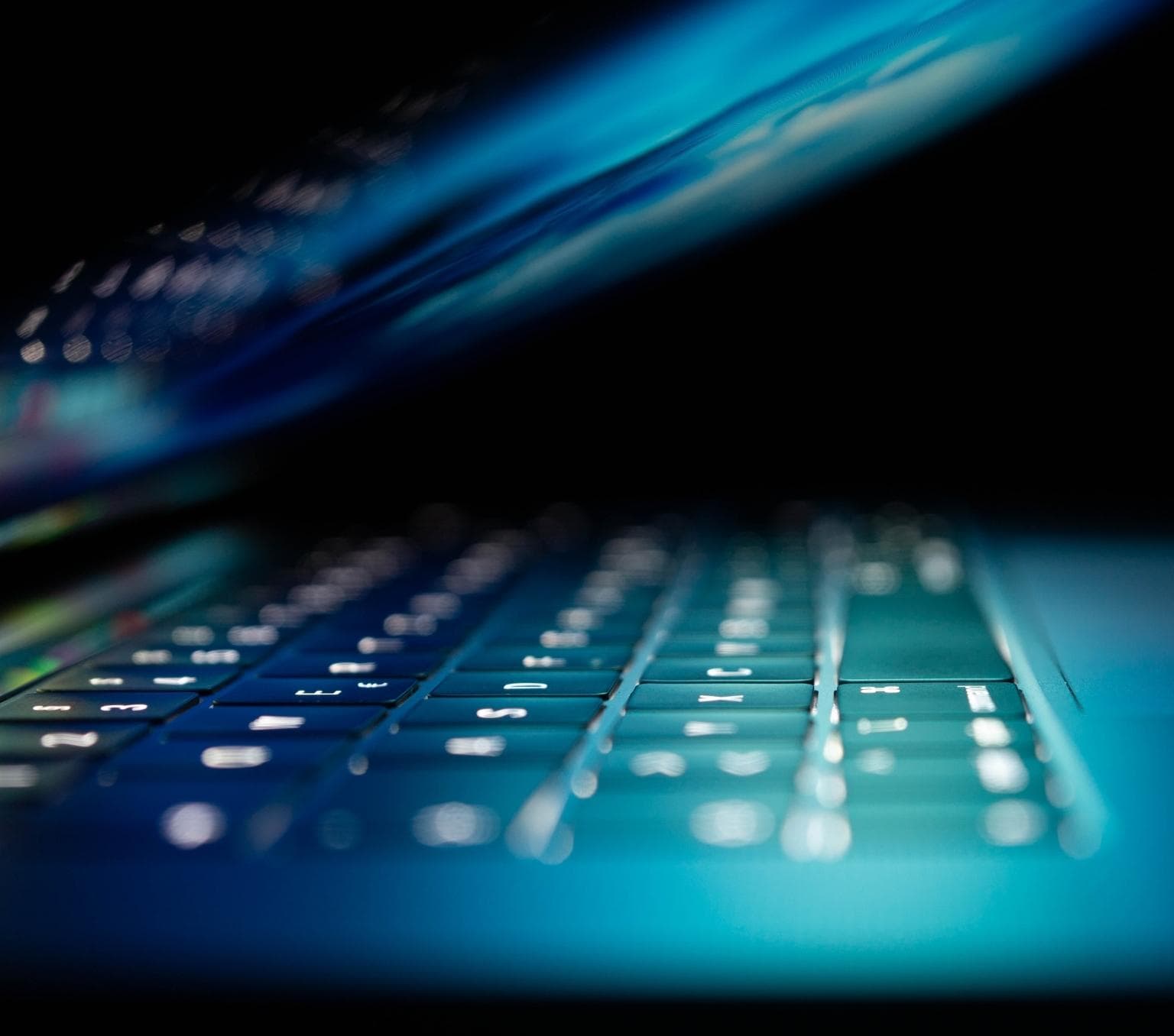 A laptop half closed with its keys illuminated. The brightness from the screen has a blue glow.