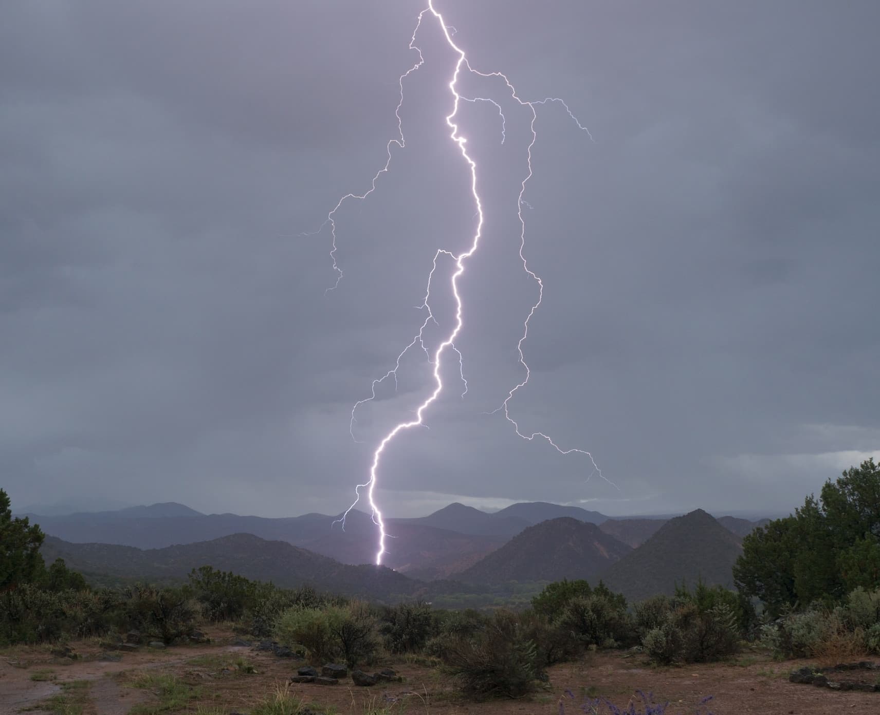 Bolt of lightning reaches from the sky into a mountain range.