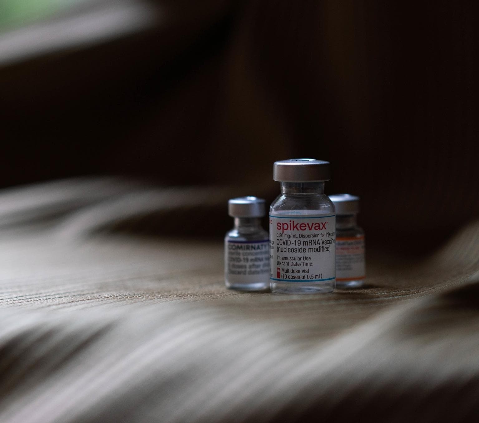 Three vials of the COVID-19 vaccine placed side-by-side. The vials say "spikevax" on them.