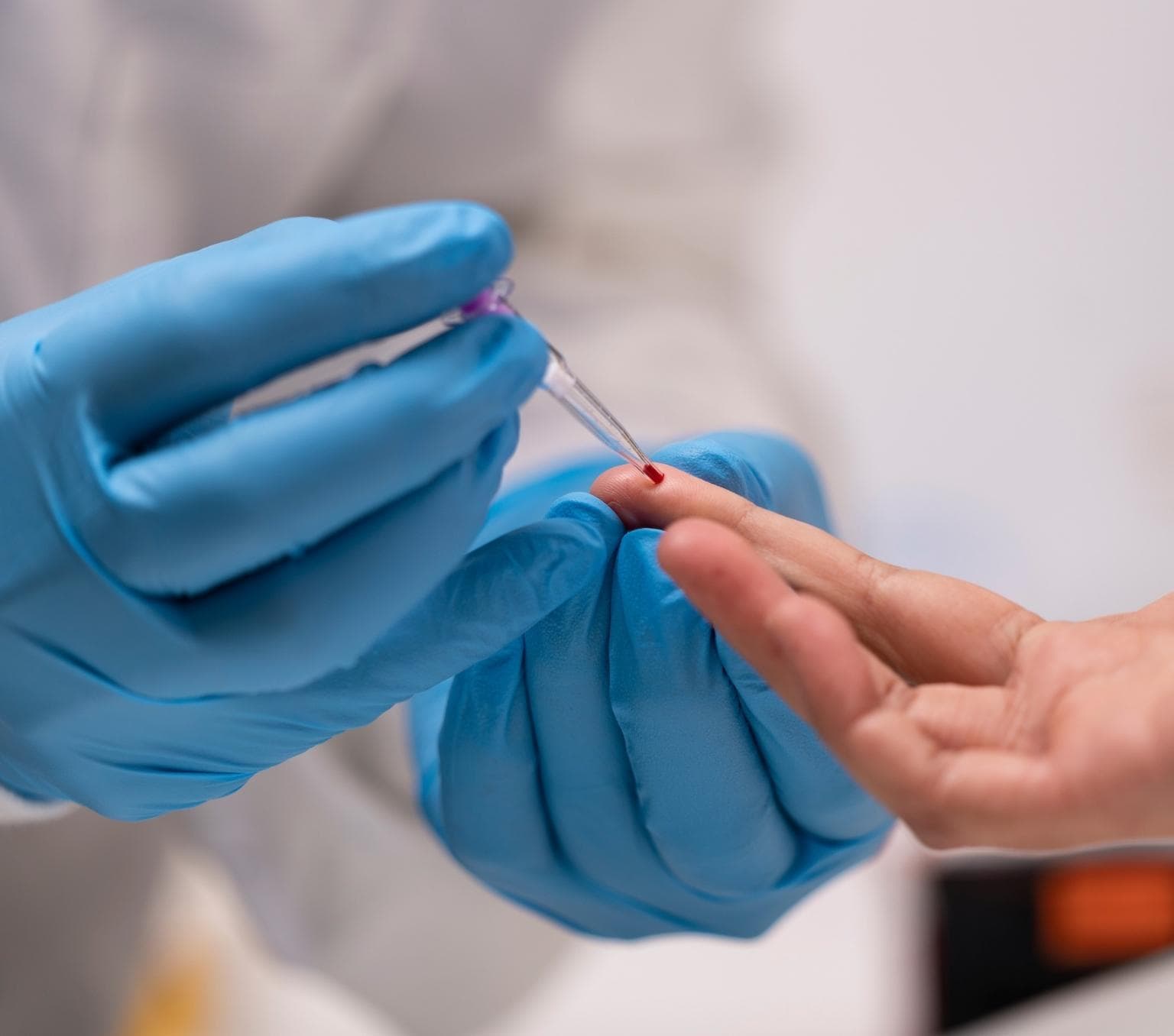 closeup of a peron's hand being held by another person's hands which are in blue gloves and holding a small medial testing device to the patient's finger