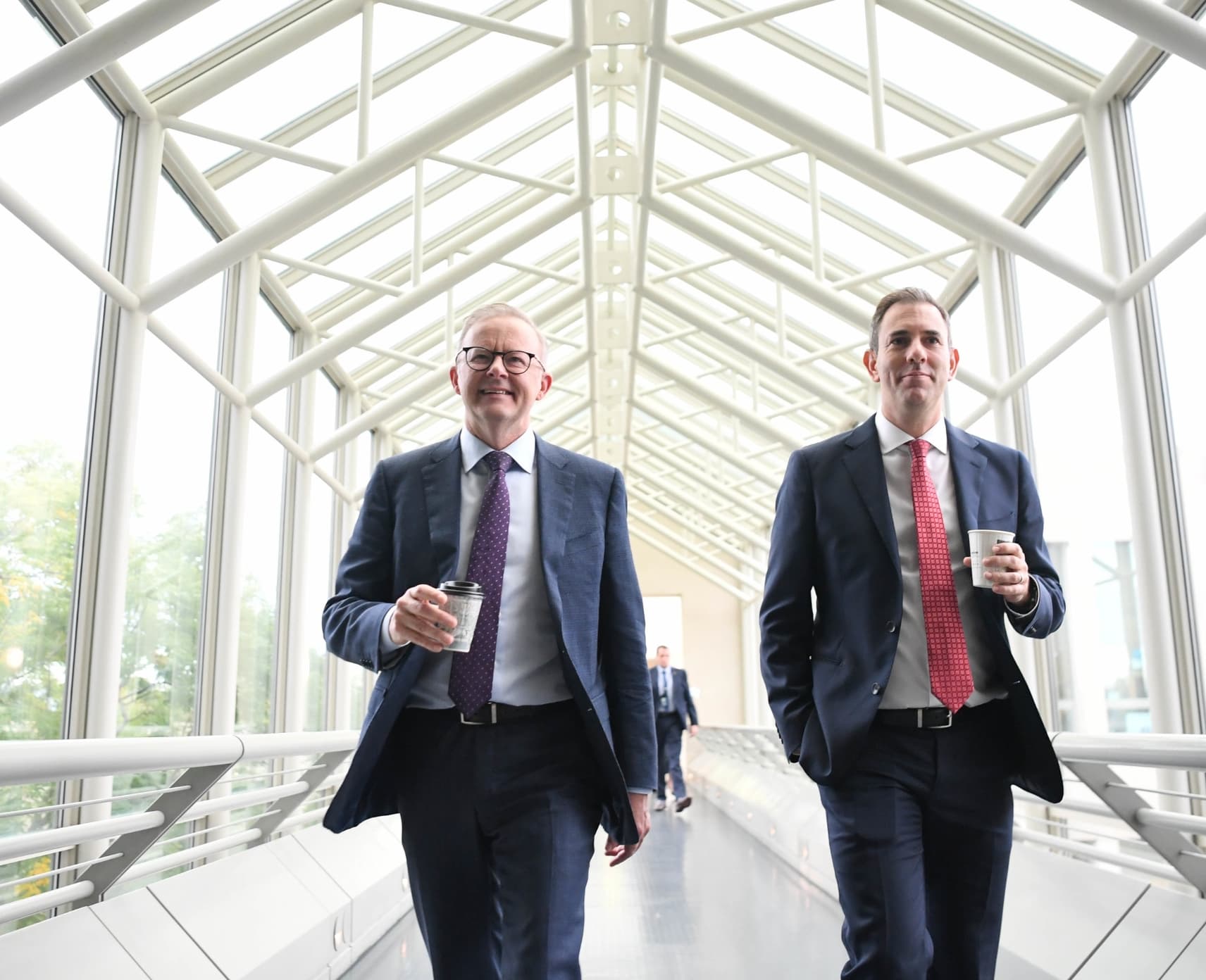 Anthony Albanese and Jim Chalmers walk along a corridor holding coffees