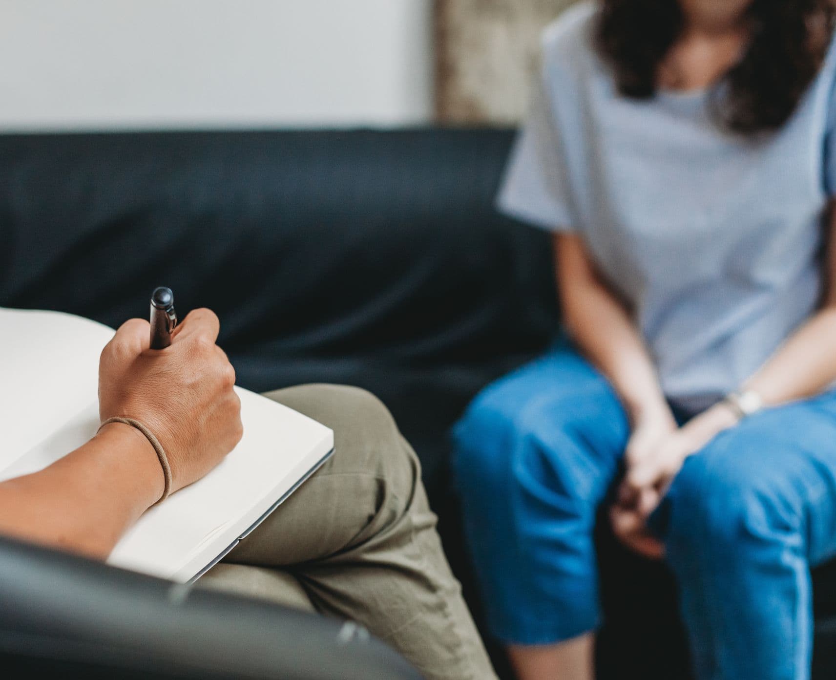 A woman sits on a couch with their hands in their lap, talking to a psychologist