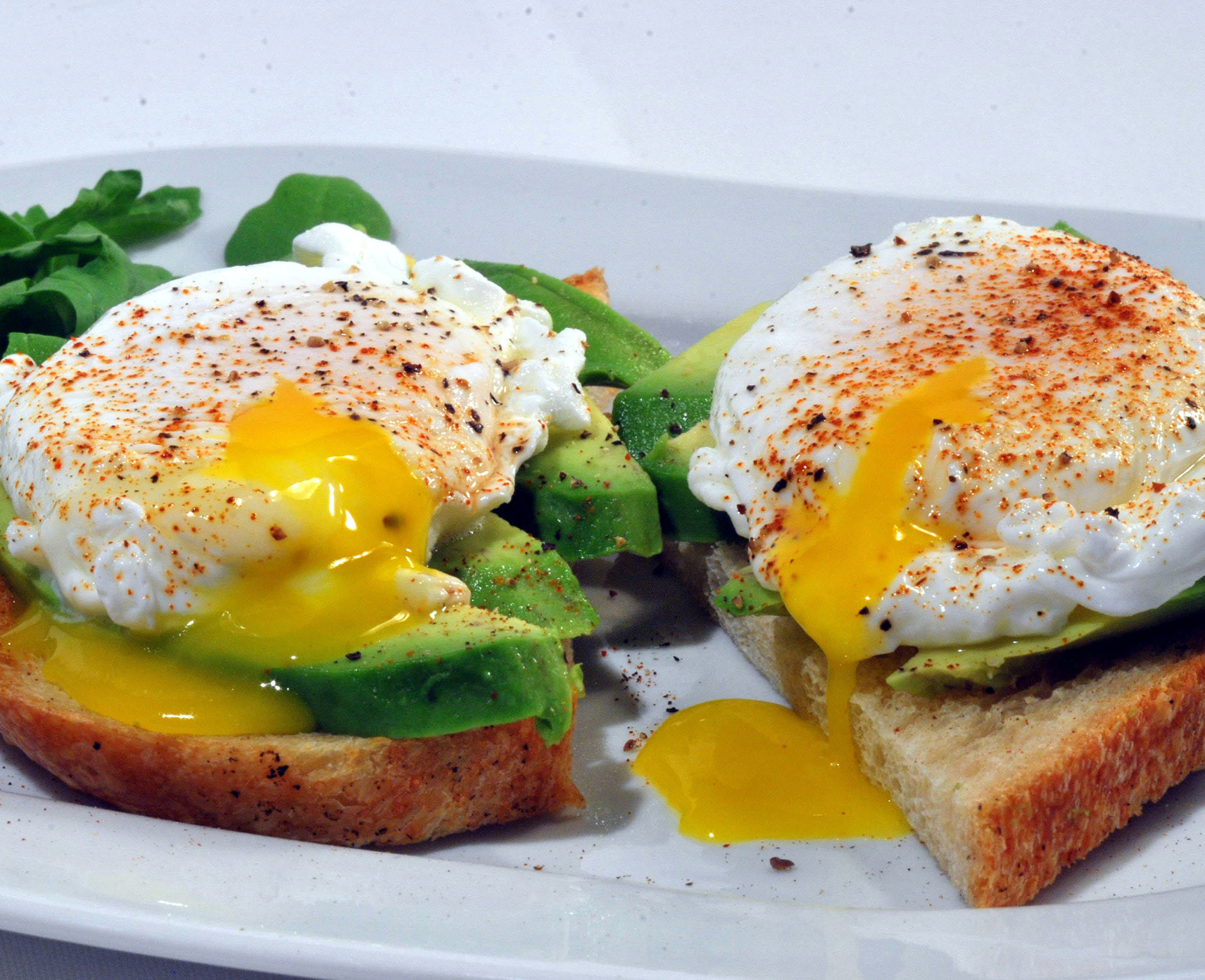Two poached eggs and smashed avocado on toast served on a plate.