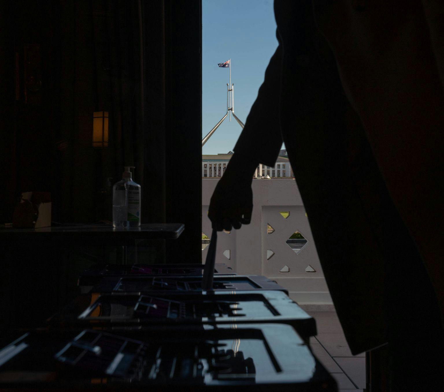 Hand placing a vote in ballot box. Parliament house is in the background.