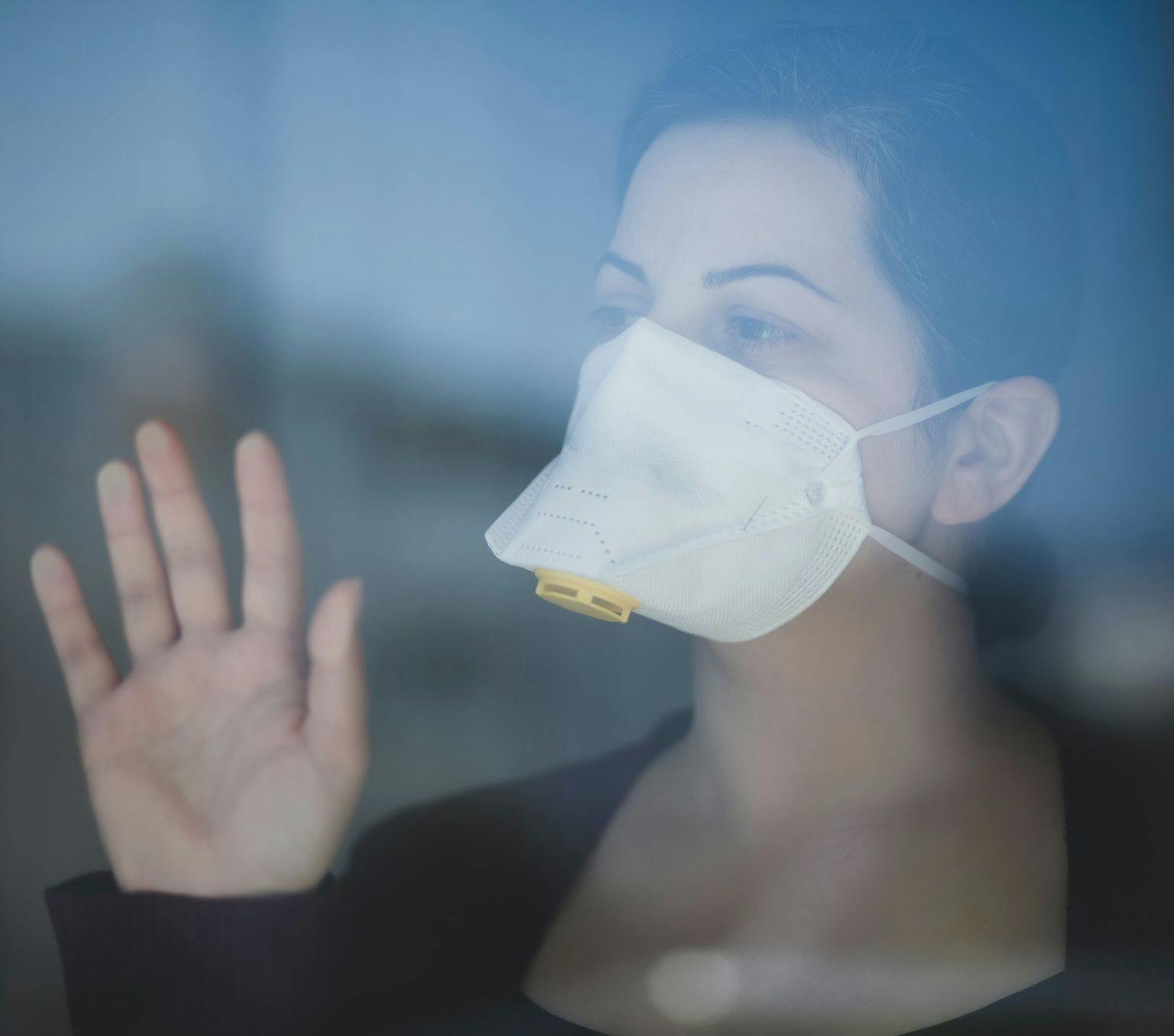 Women wearing a mask looking through a window.