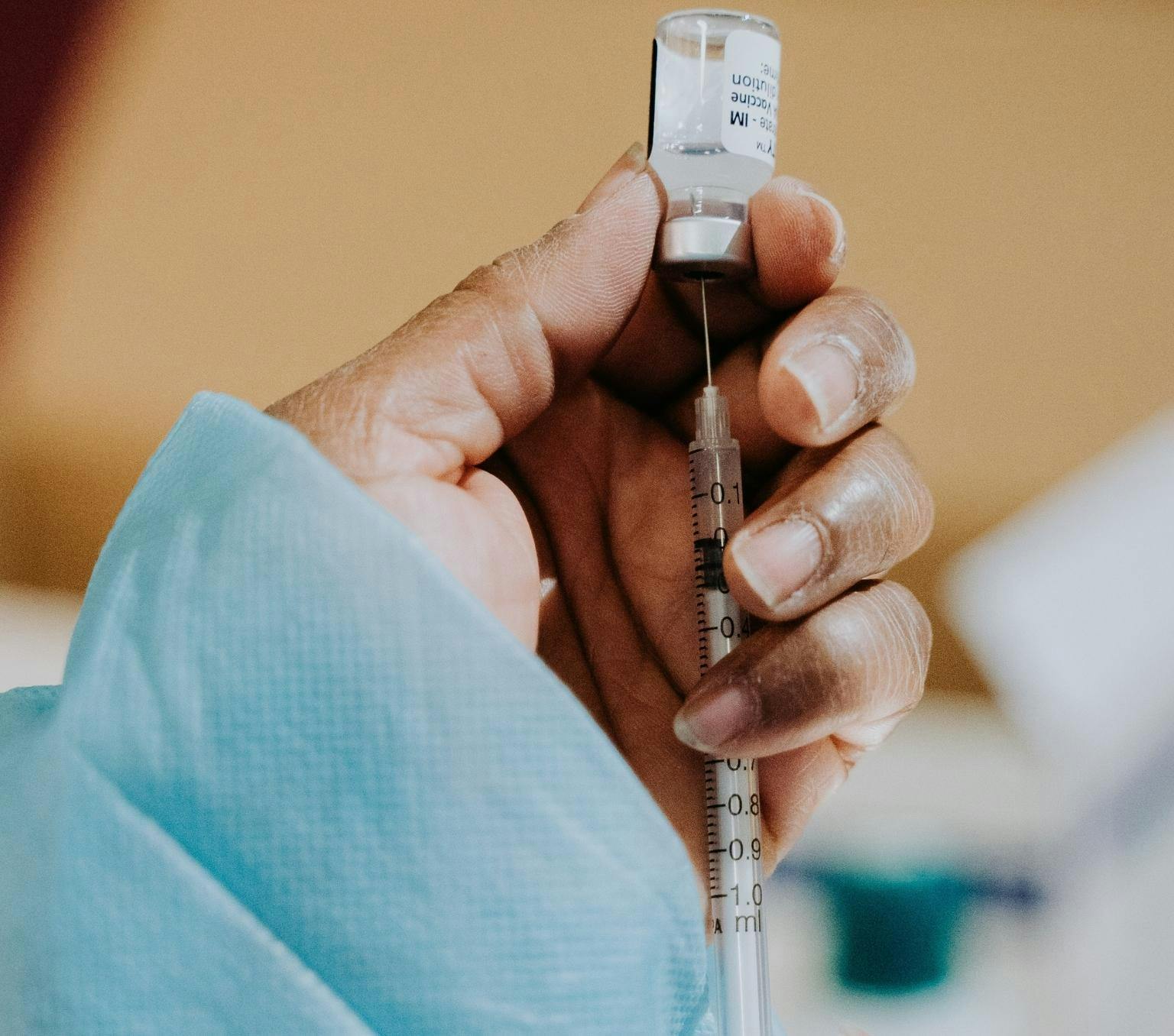 close up on a person's hands. The have a blue sleeve showing and are drawing liquid from a vaccine vial into a syringe