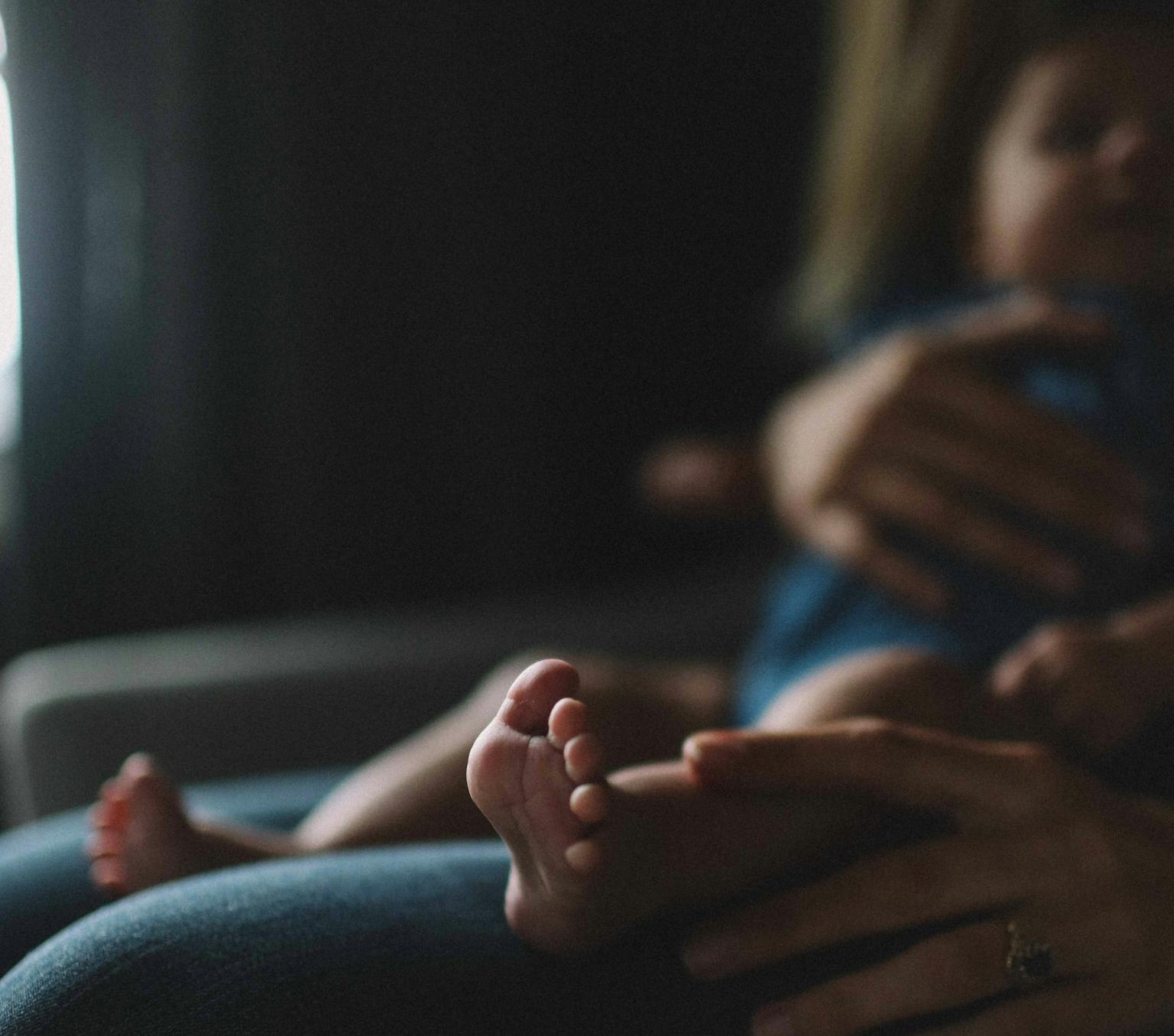 a babies foot is in the foreground and a baby is sitting on its mother's lap