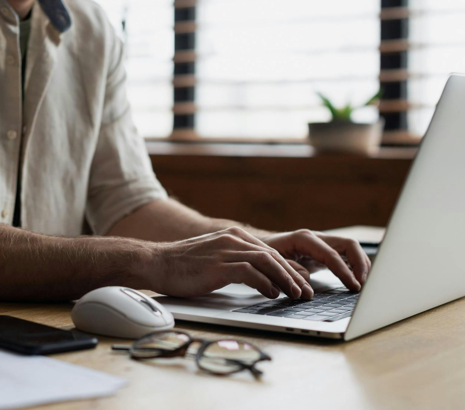 close-up of a person's hands typing on a laptop at a desk.