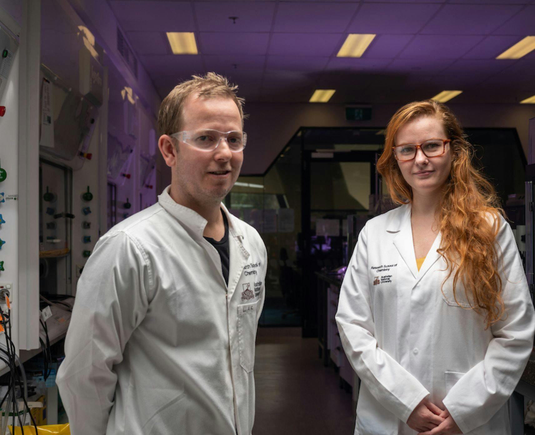 Luke Connal and Jekaterina Viktorova from Syenta stand next to each other in their lab. They're wearig white lab coats.