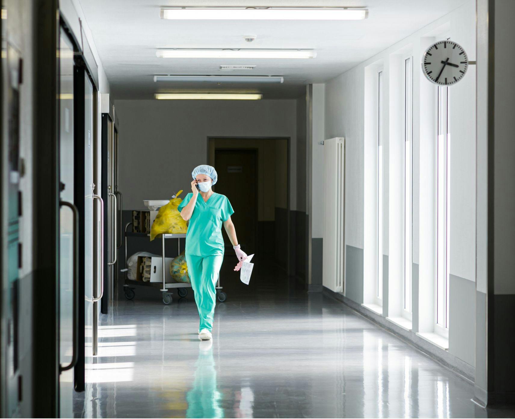 A medical professional in scrubs walking in hospital while on the phone.