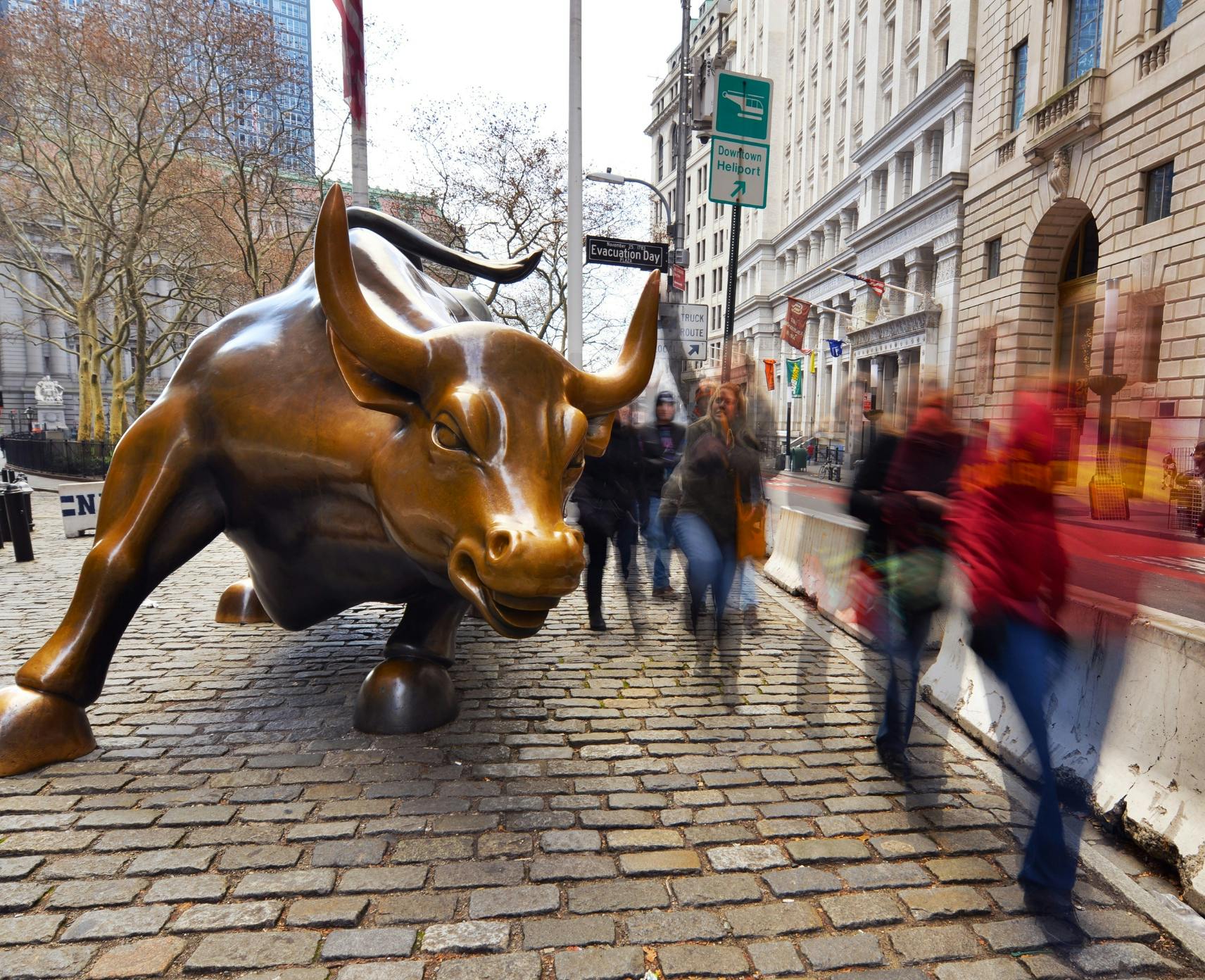 Wall Street charging bull statue and the blurred figures of crowds around it. Picking winners with Joseph Stiglitz