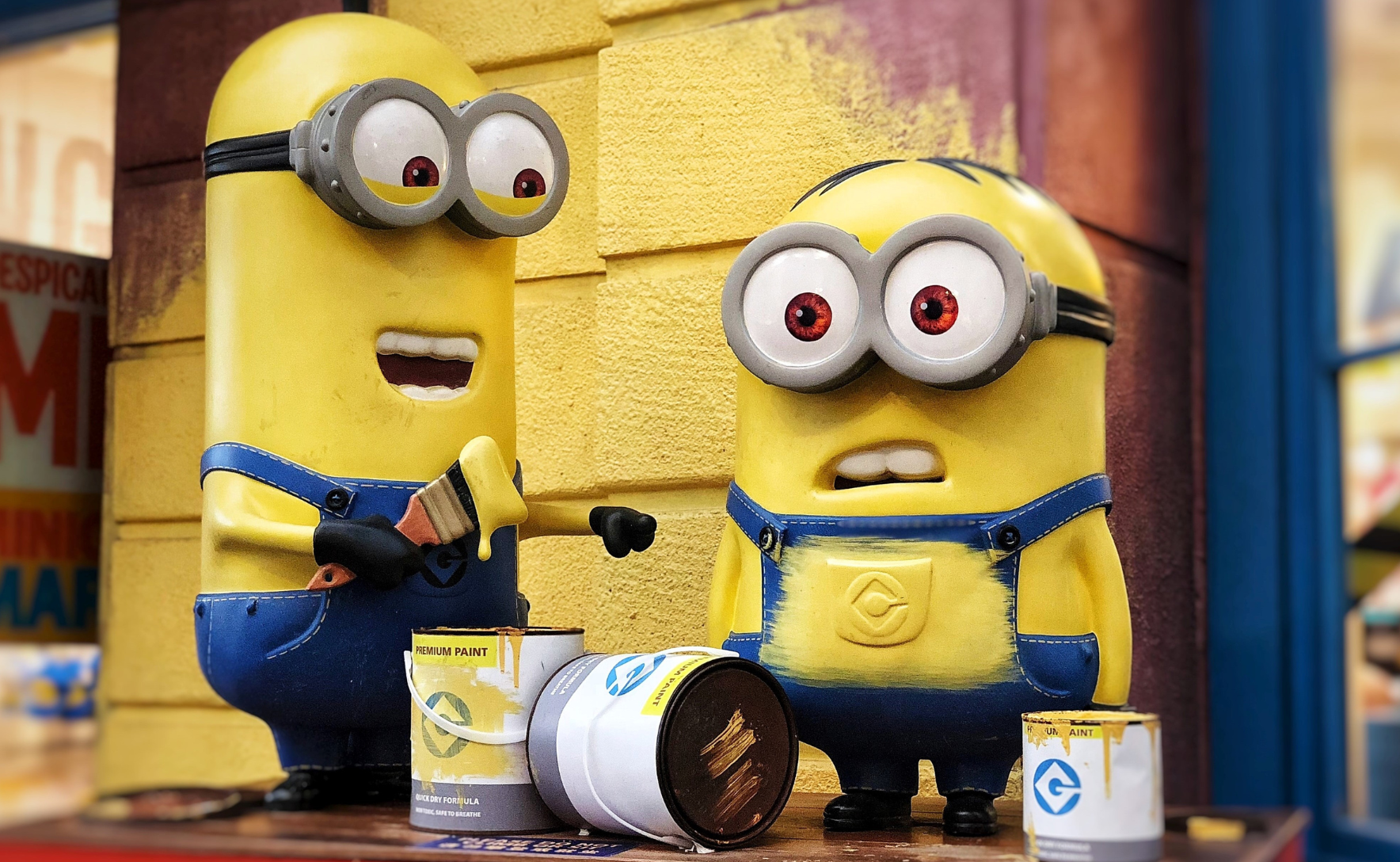 Two Minions in blue overalls standing with cans of yellow paint.