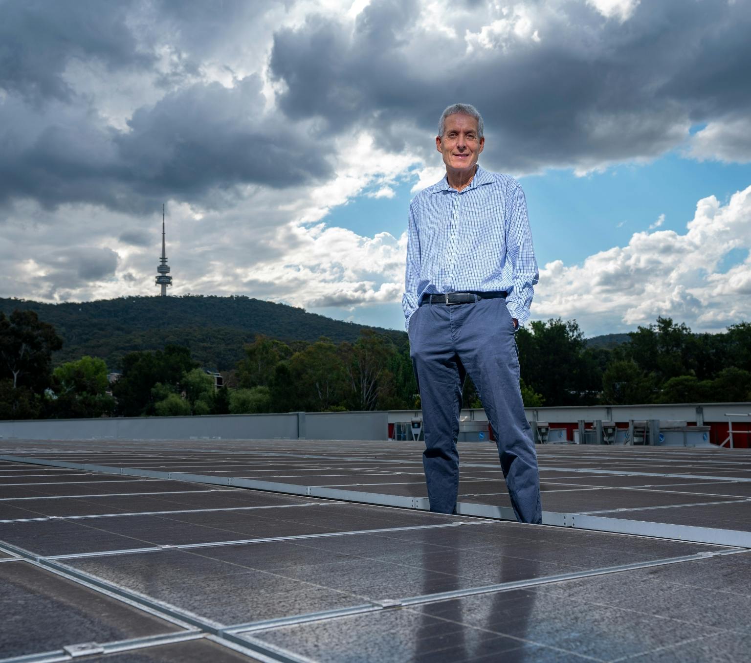 Professor Andrew Blakers standing next to solar panels. He is wearing a blue shirt and he has his hands in his pockets.