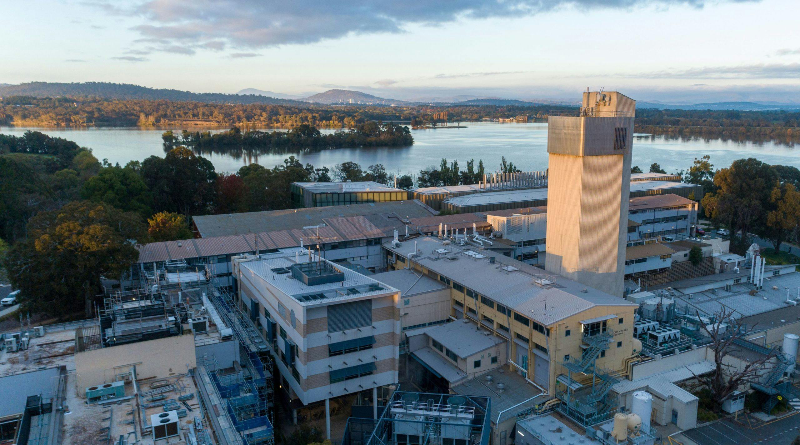 An aerial view of the ANU Research School of Physics, showing the tops of buildings and a large ivory tower rising up. Lake Burley Griffin is seen in the distance.